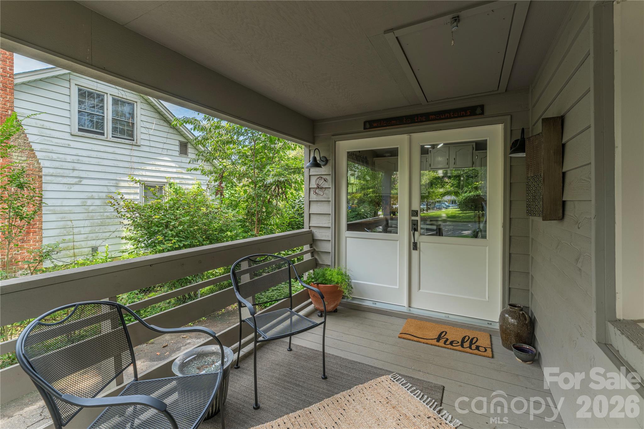 Covered porch with black metal chairs, potted plants, and white glass-paneled double doors.
