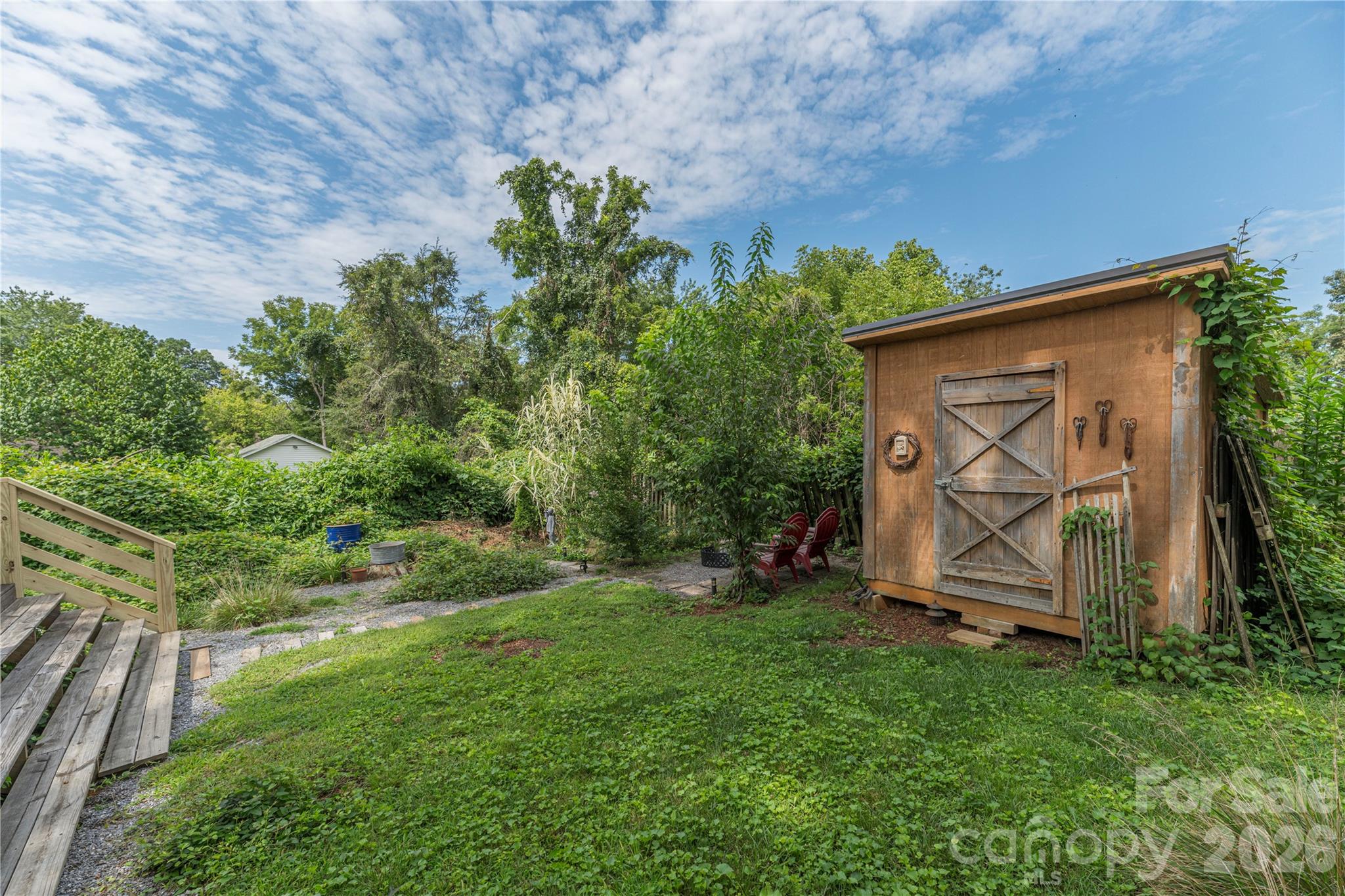 Backyard with a wooden shed, gravel path, deck steps, and red Adirondack chairs.