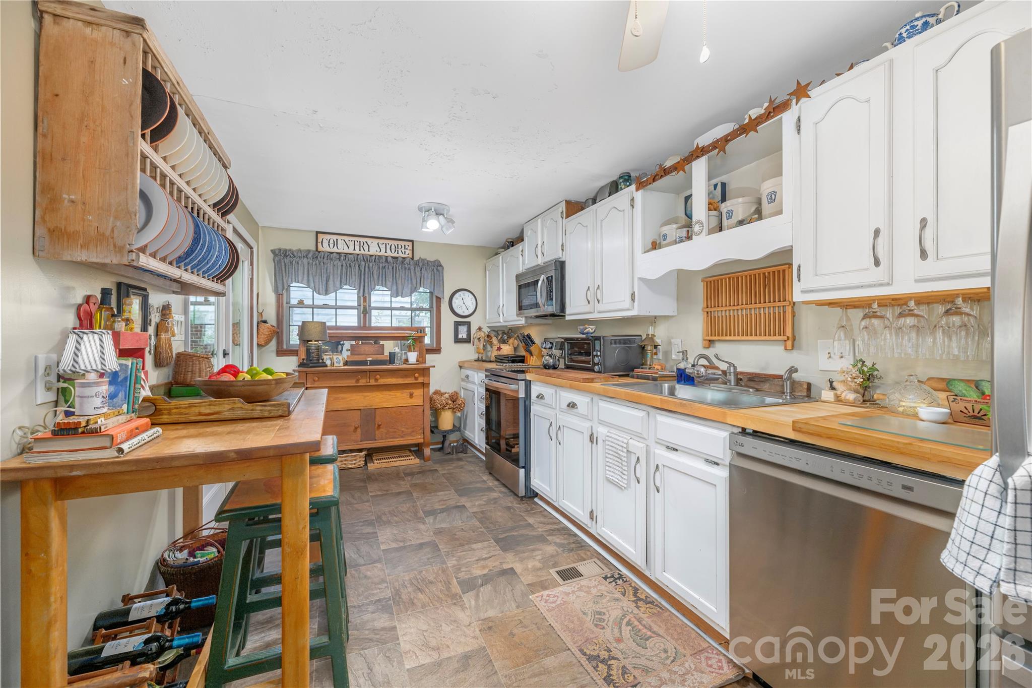 Kitchen with white cabinets, wooden countertops, stainless steel appliances, and open dish racks.