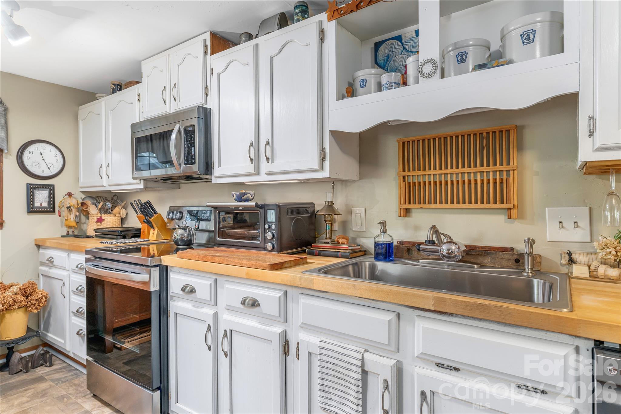 Kitchen with white cabinets, wood countertops, stainless steel appliances, and a large double-basin sink.