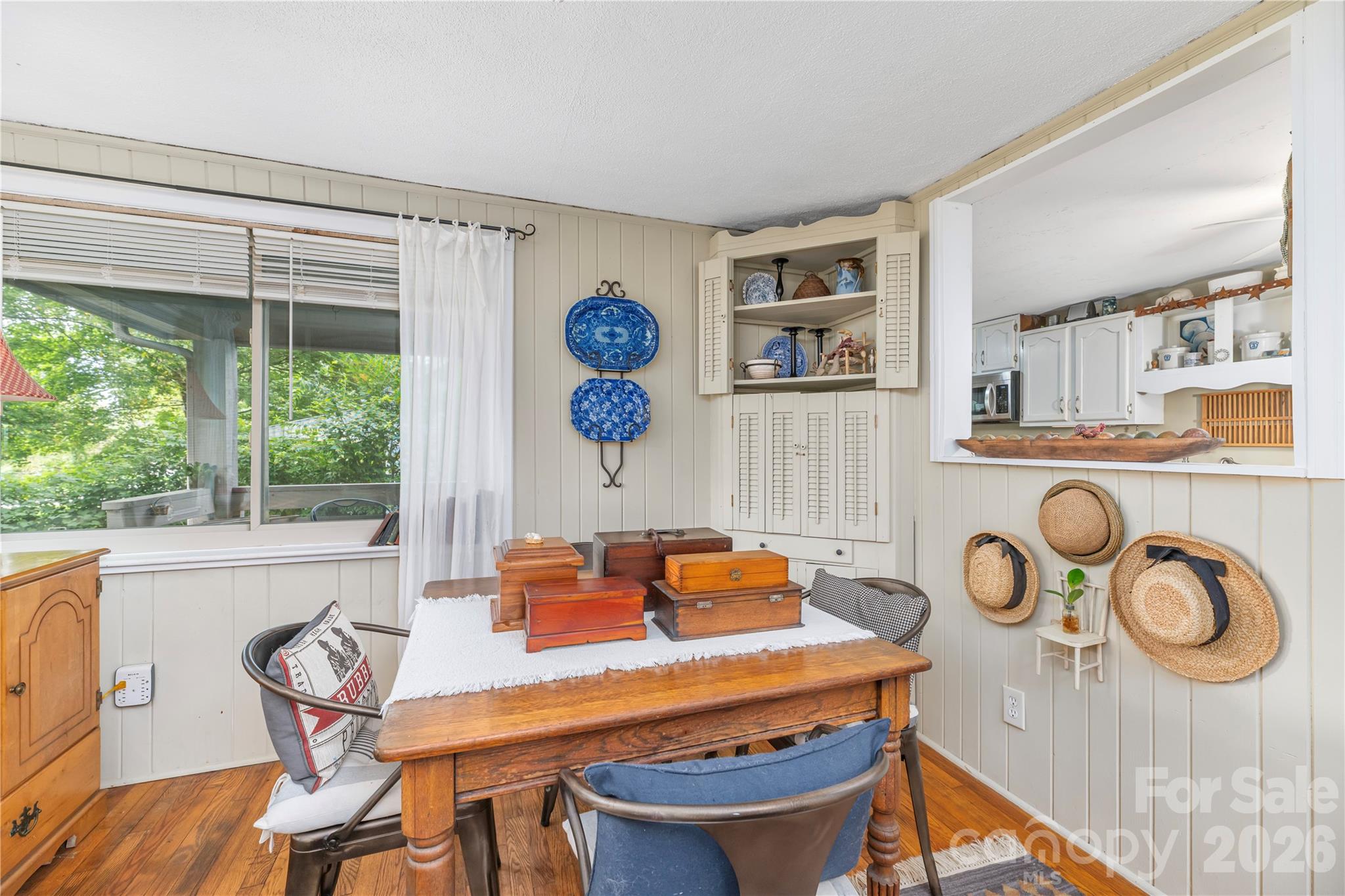 Dining area with a wooden table, built-in cabinets, and a large window overlooking greenery.