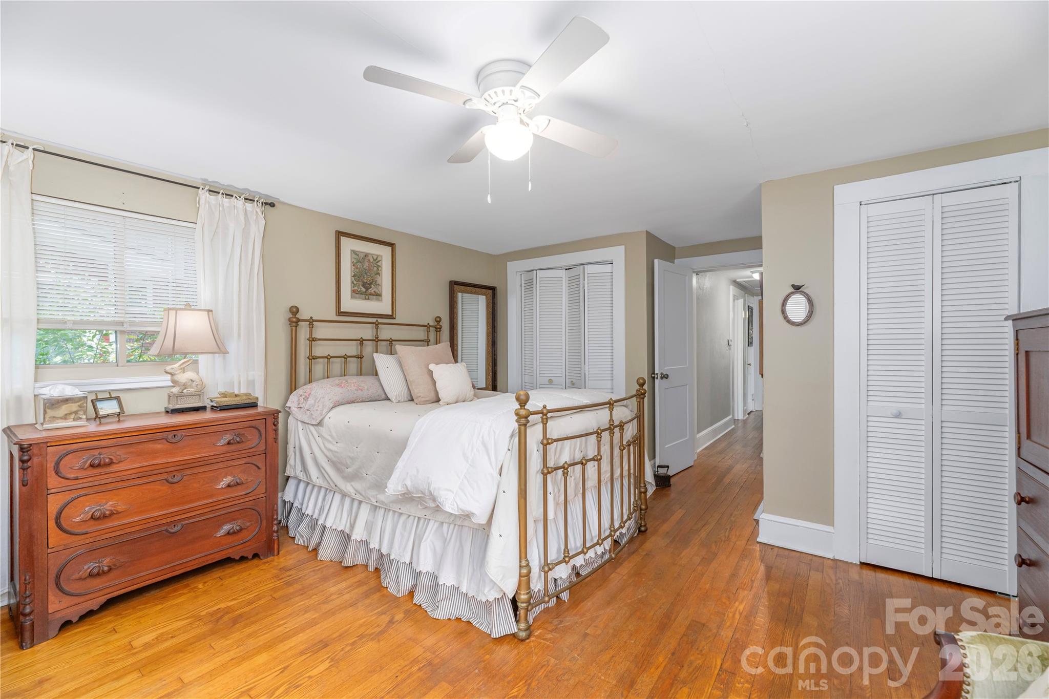 Furnished bedroom with a brass bed, hardwood floors, and white louvered closet doors.