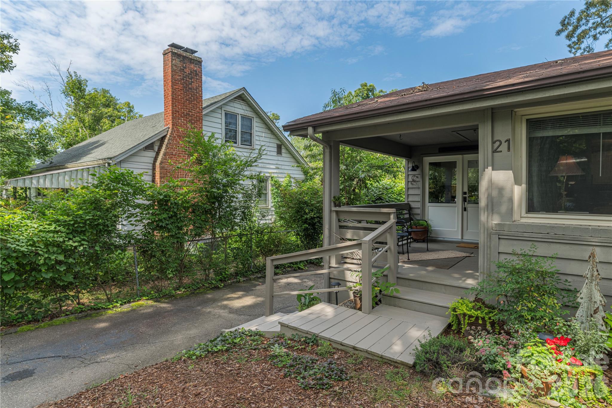 Gray-sided home with a covered front porch, entry ramp, and leafy garden.