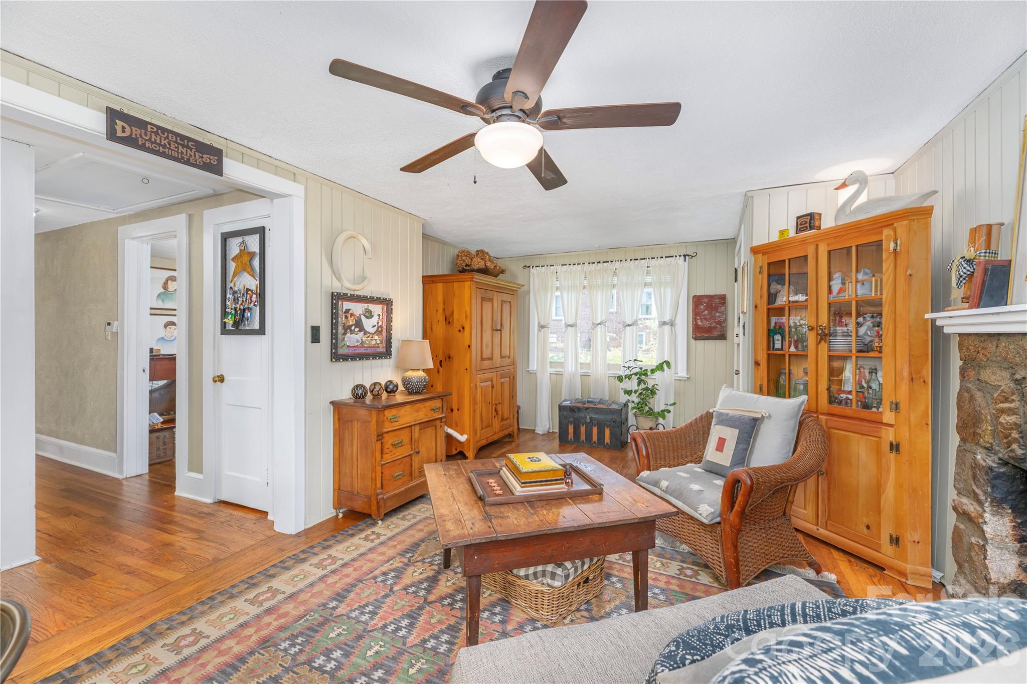 Bedroom with a wicker armchair, pine cabinets, patterned rug, and stone fireplace.