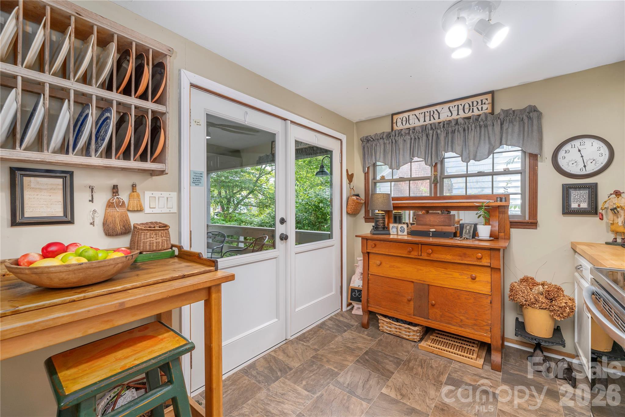 Kitchen with a wooden plate rack, fruit bowl, glass-paneled door, and antique dresser beneath curtained windows.