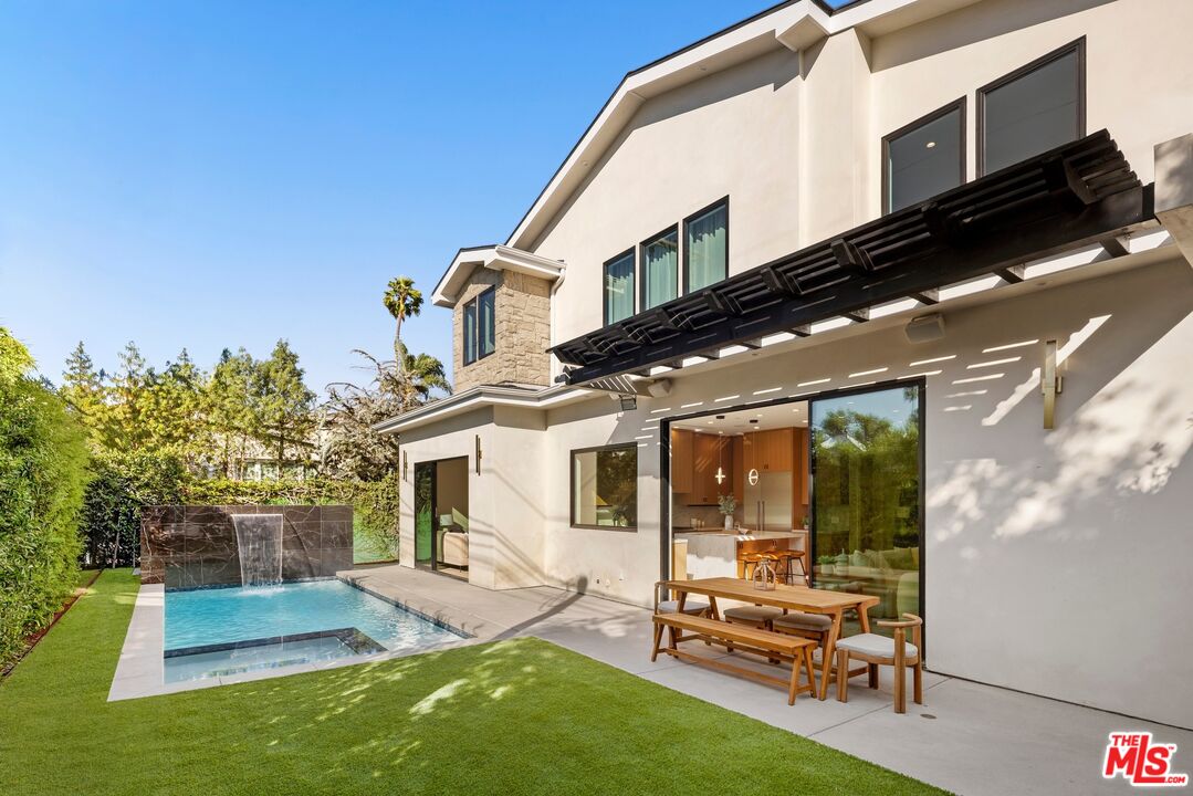 Modern two-story home with a pool and waterfall, lawn, and pergola-shaded patio.