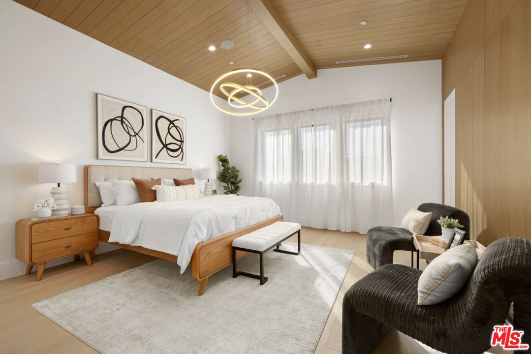 Bedroom with a wood-plank ceiling, ring chandelier, king-size bed, and dark lounge chairs.