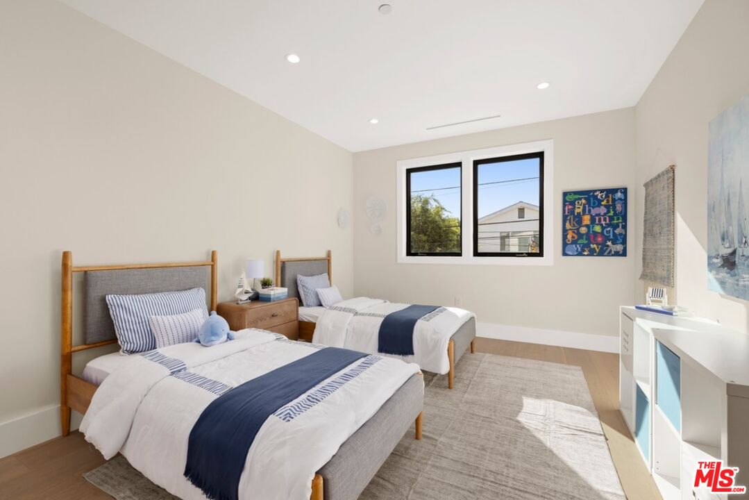 Staged bedroom with two single beds, navy-and-white bedding, and a large window.