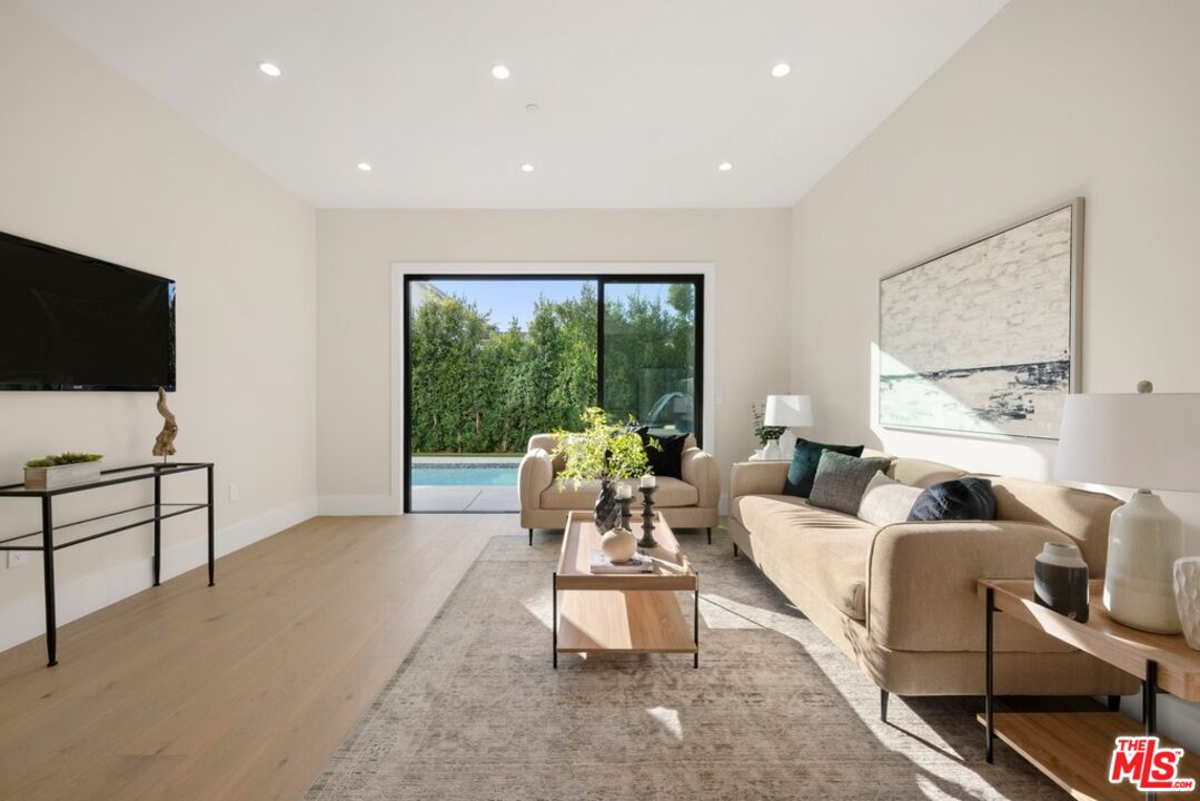 Staged living room with beige seating and sliding doors opening to a poolside patio.
