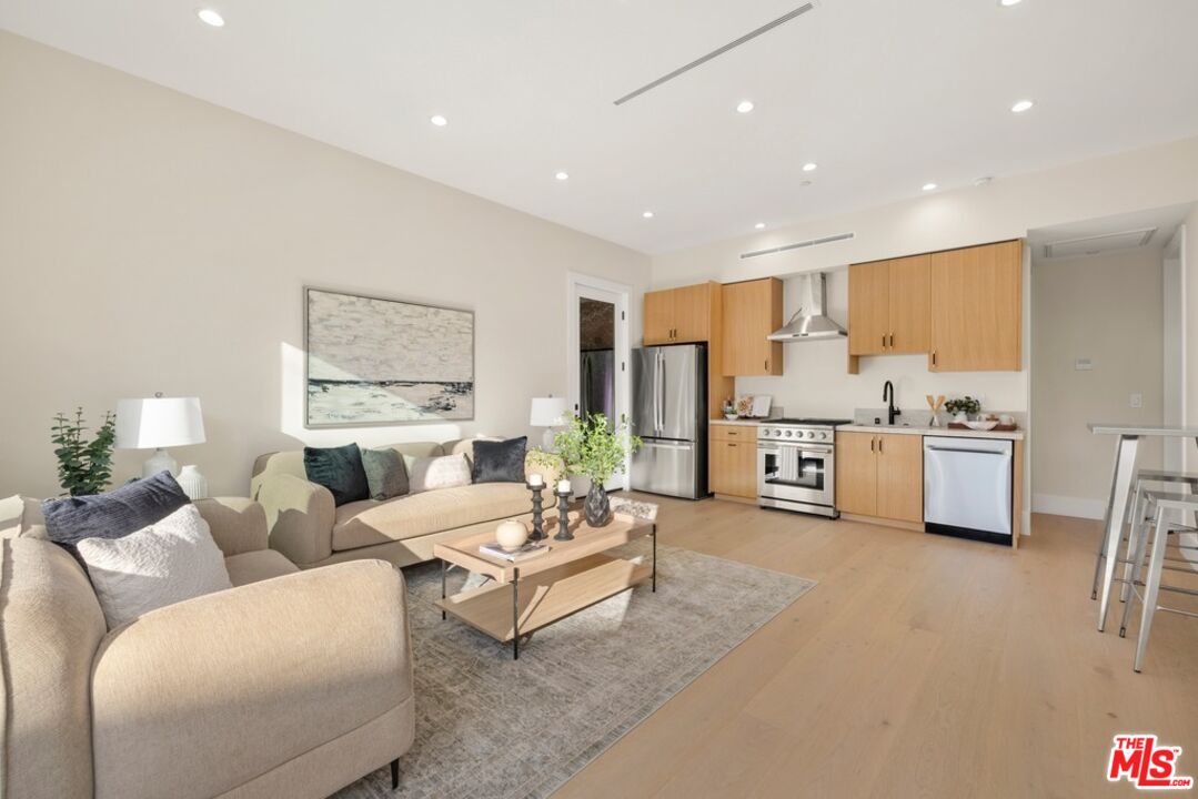 Open-plan living room and kitchen with a beige sectional, light wood floors, and wood cabinetry.