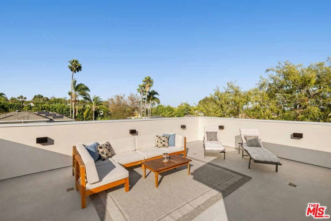 Rooftop terrace with a white sectional, cushioned loungers, and palm trees beyond the parapet.