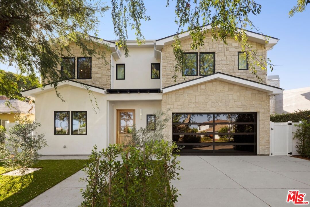 Two-story stone-and-stucco house with black-framed windows, a dark garage door, and a broad driveway.