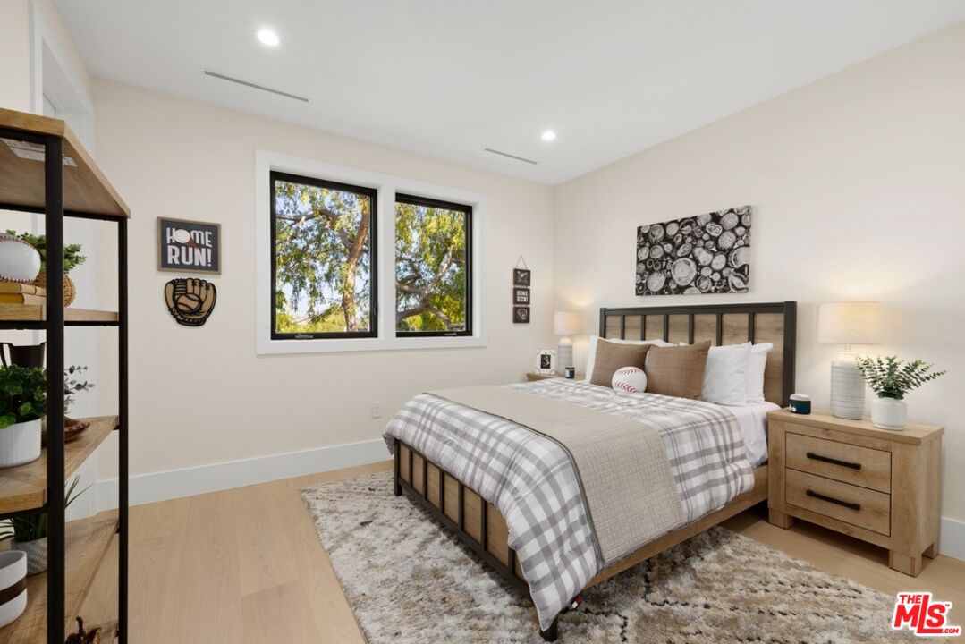 Staged bedroom with plaid bedding, baseball decor, and two windows overlooking leafy trees.