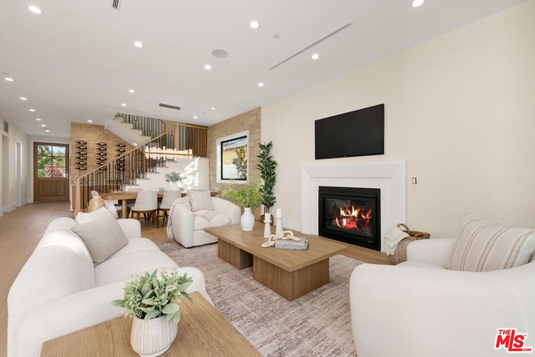 Living room with white sofas, a fireplace, and an open dining area beside the staircase.