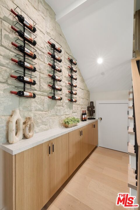 Wine room with wall-mounted racks on a stone wall above light wood cabinetry.