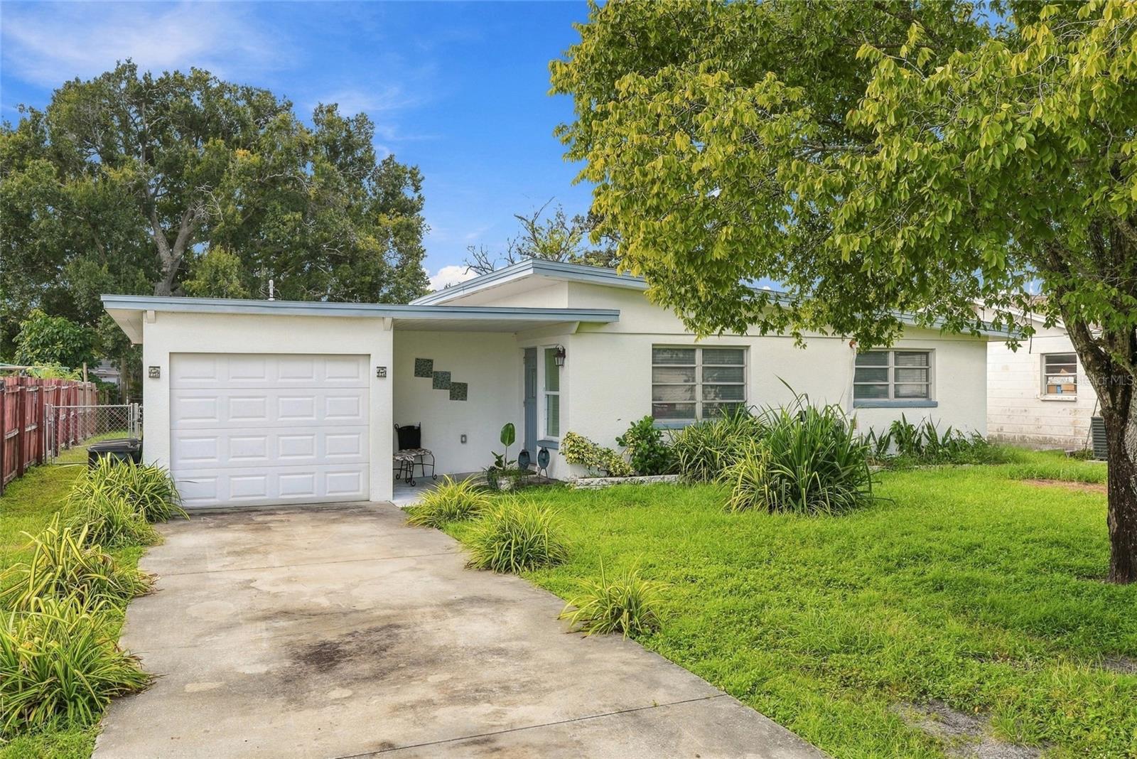 Single-story white house with an attached garage, covered entry, and tree-shaded lawn.