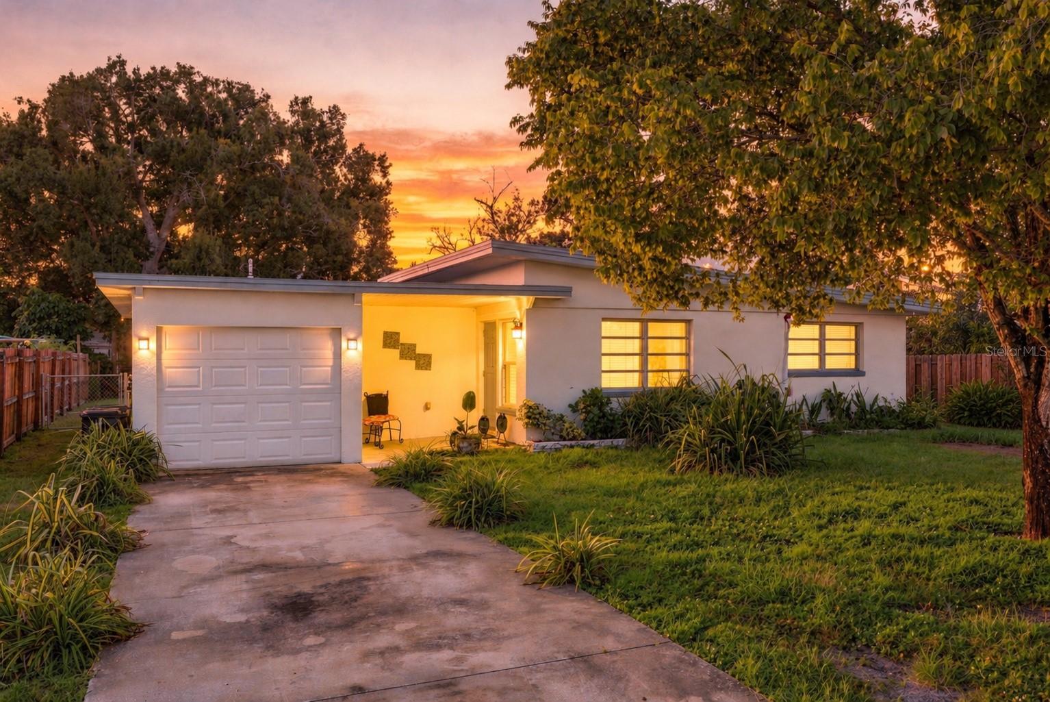 Single-story home with an attached garage and landscaped yard under a vivid sunset.