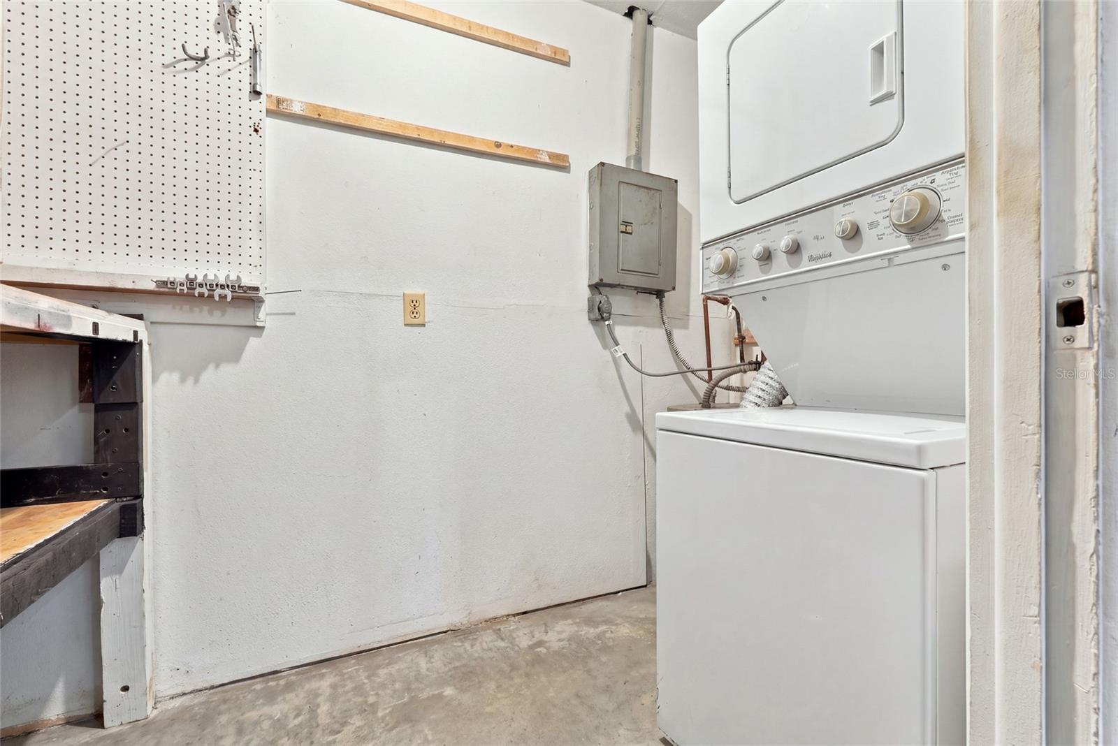 Laundry room with a stacked washer and dryer beside a pegboard and workbench.