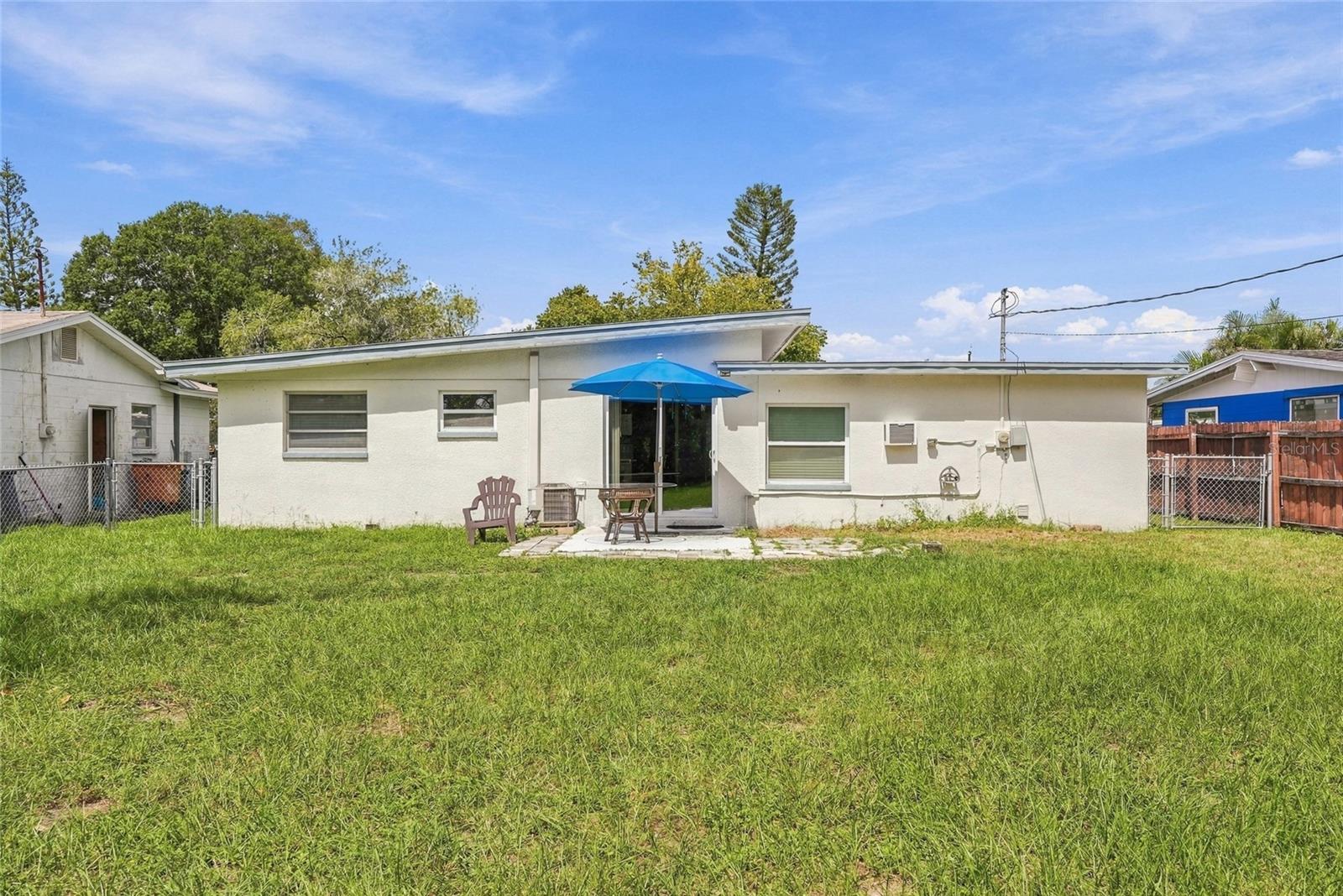 Single-story home's rear exterior with a grassy yard and a patio shaded by a blue umbrella.
