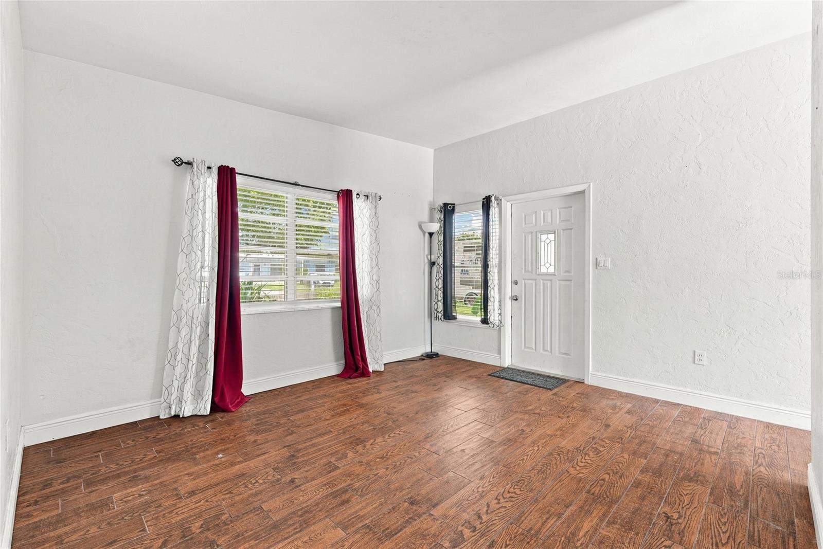 Unfurnished living room with wood-look floors, two curtained windows, and a white front door.