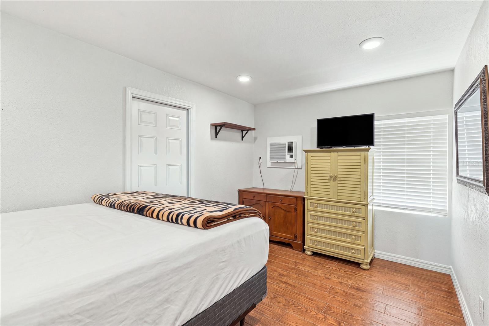 Furnished bedroom with a striped blanket, yellow dresser, television, and window blinds.