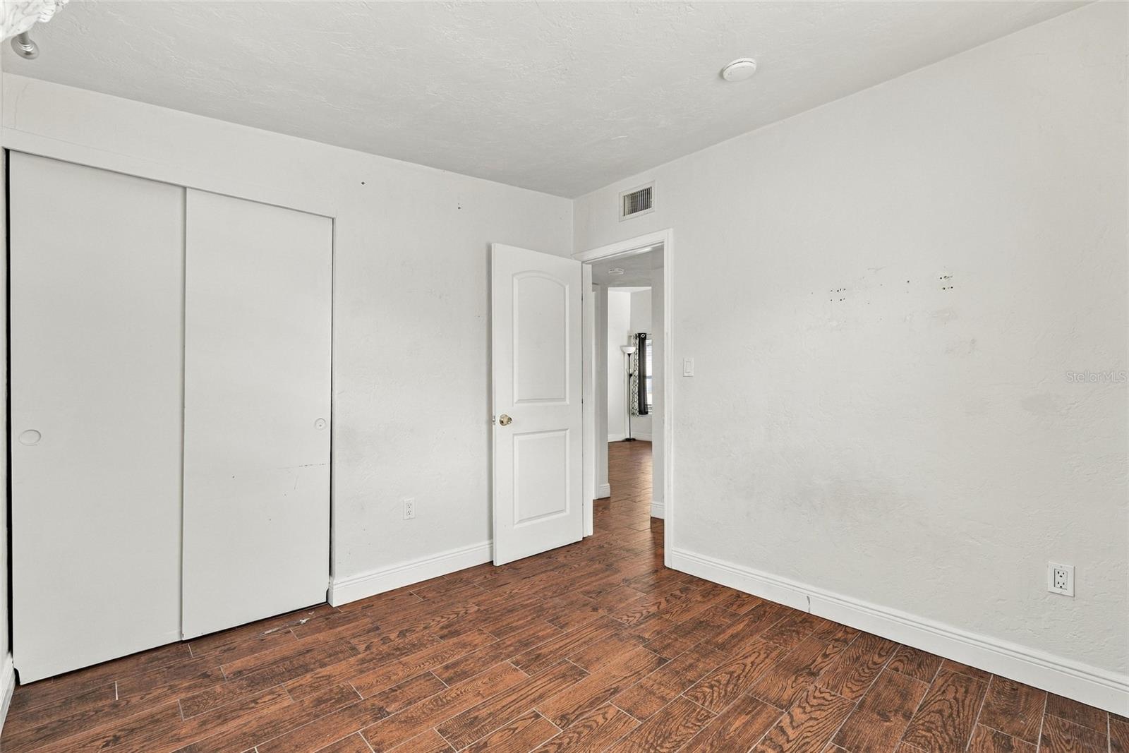 Empty bedroom with a sliding-door closet, brown wood-look tile, and an open doorway.