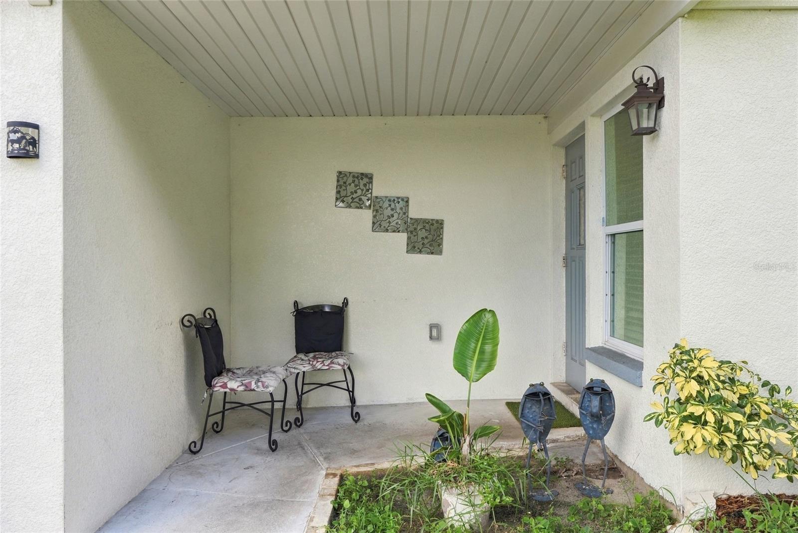 Covered front porch with metal chairs, a gray entry door, and potted plants.