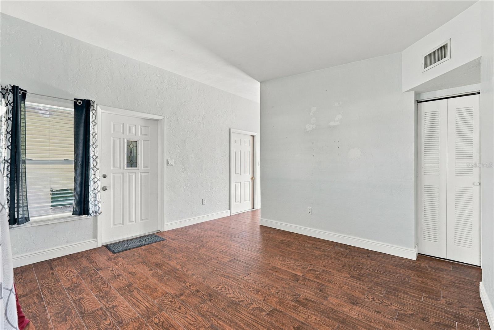 Empty room with wood-look tile flooring, a curtained window, entry door, and louvered closet doors.
