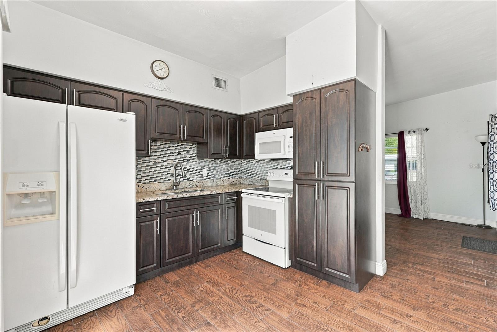 Kitchen with dark wood cabinets, granite counters, mosaic backsplash, and white appliances.