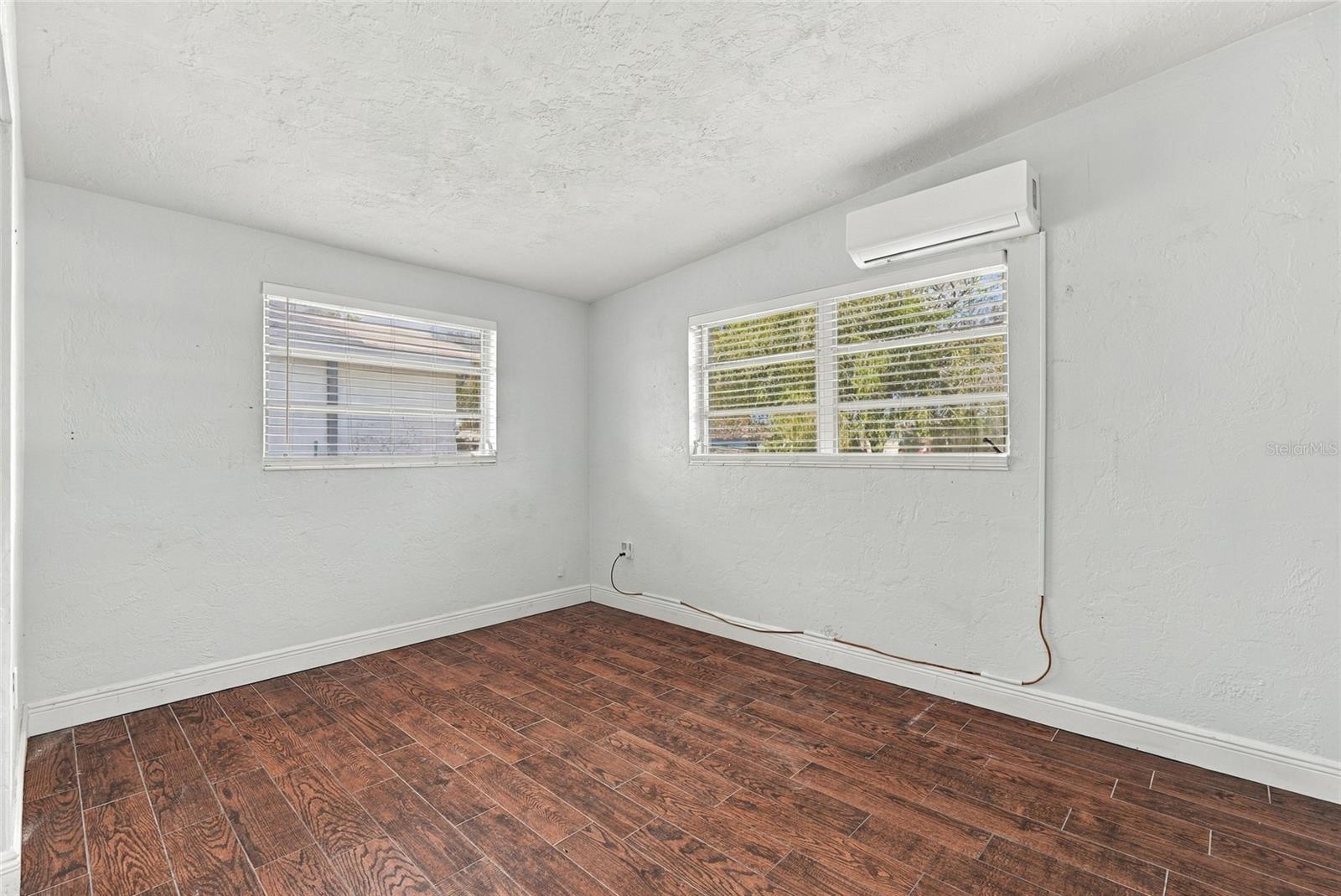 Vacant room with two blinded windows, a wall-mounted mini-split, and wood-look tile flooring.