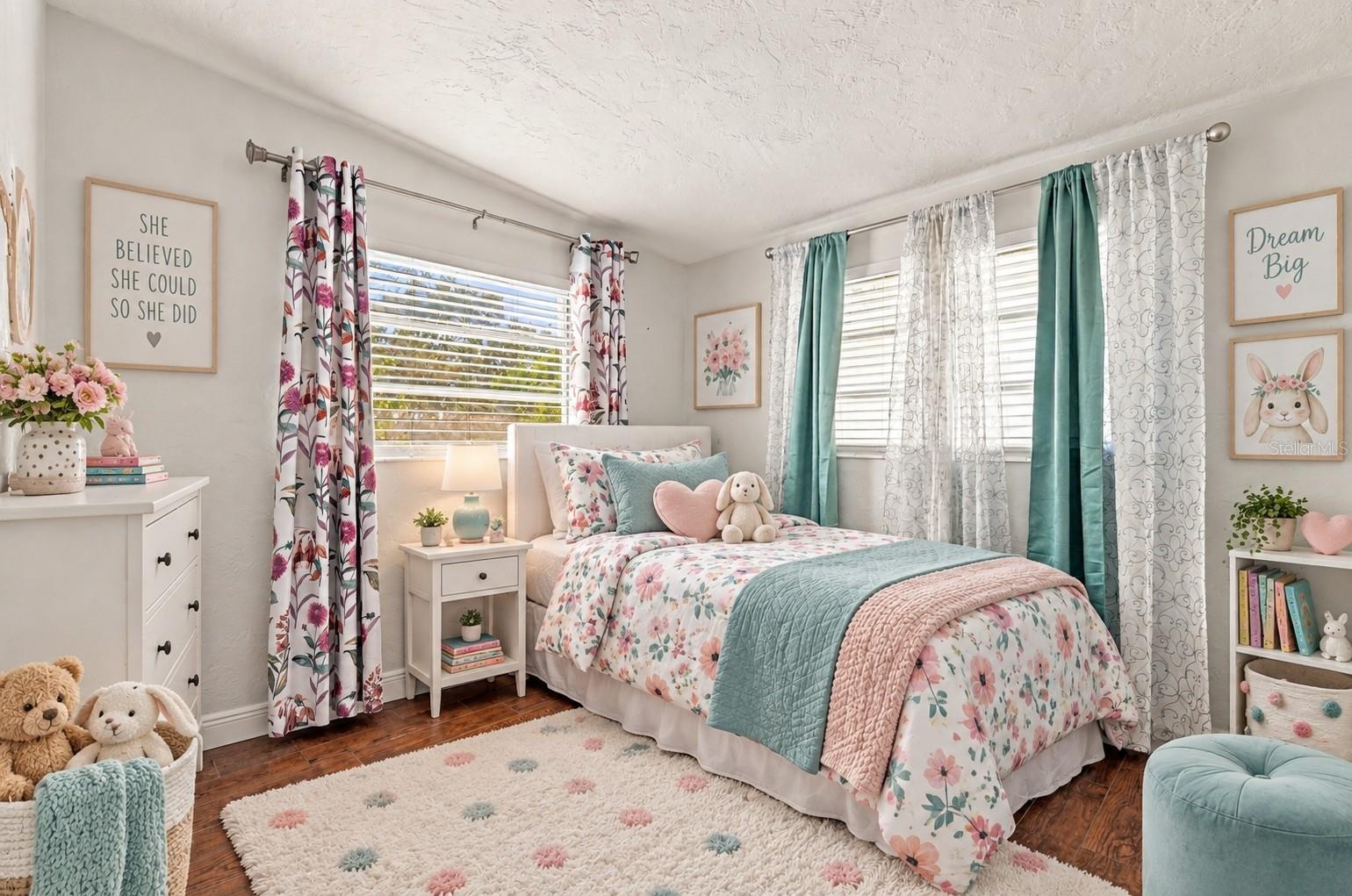 Bedroom with floral bedding, teal accents, two curtained windows, and plush toys.