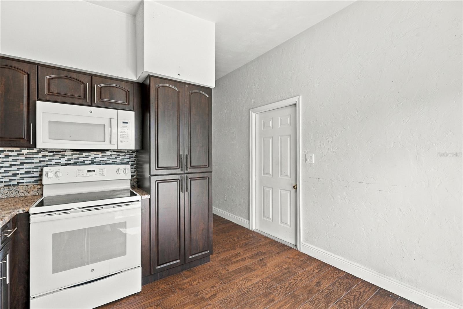 Kitchen with dark wood cabinets, white appliances, mosaic tile backsplash, and wood-look flooring.
