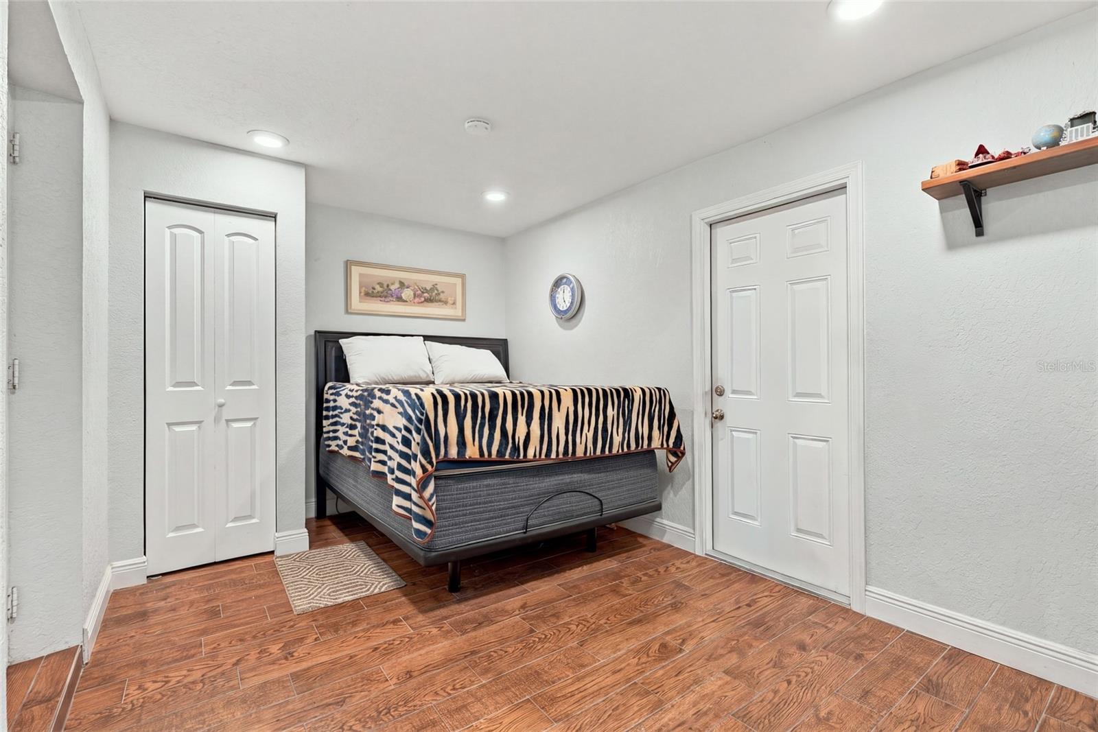 Bedroom with a striped bedspread, wood-look tile flooring, and white closet and entry doors.