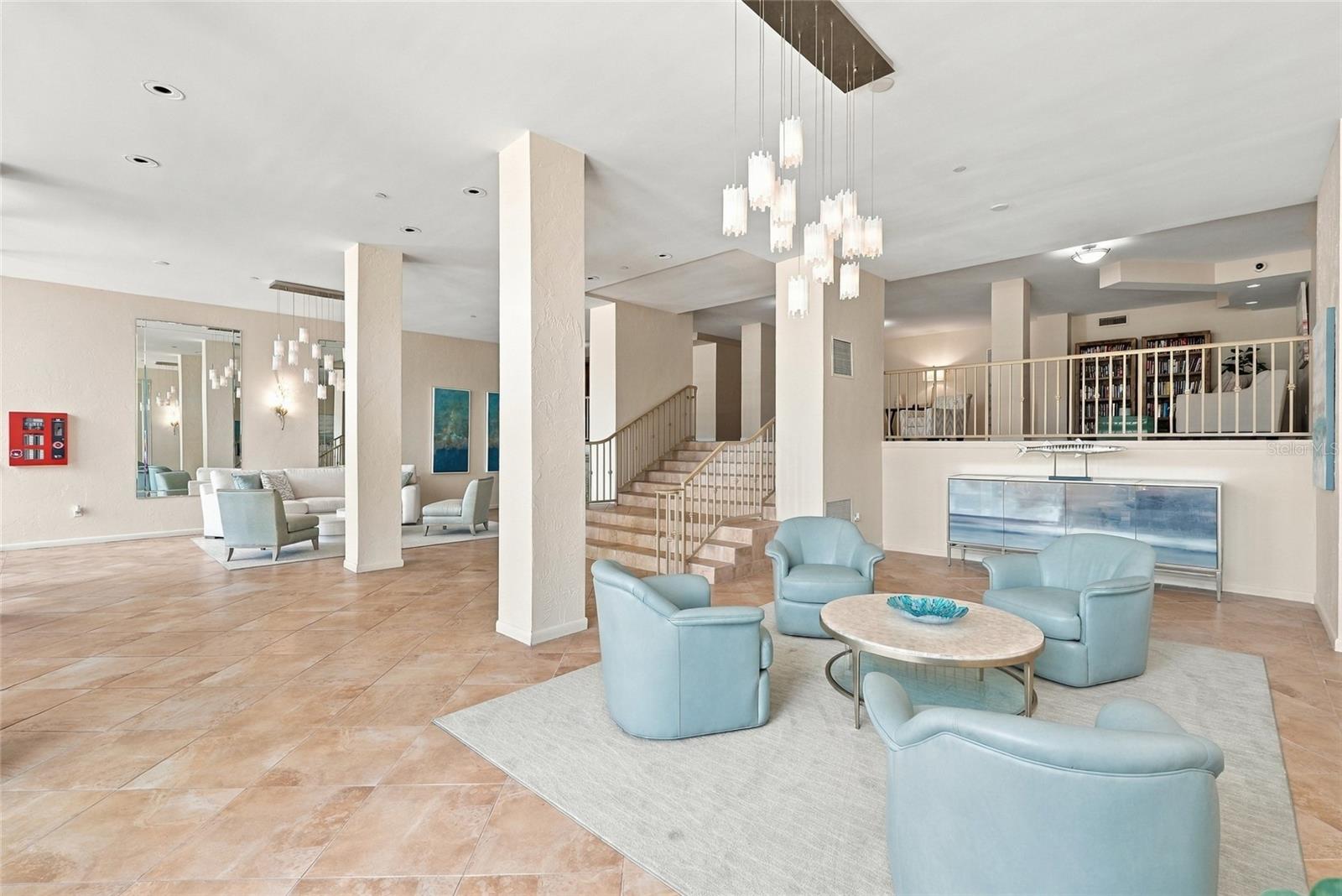 Furnished lounge with pale blue chairs, tiled floors, pendant lights, and a staircase.