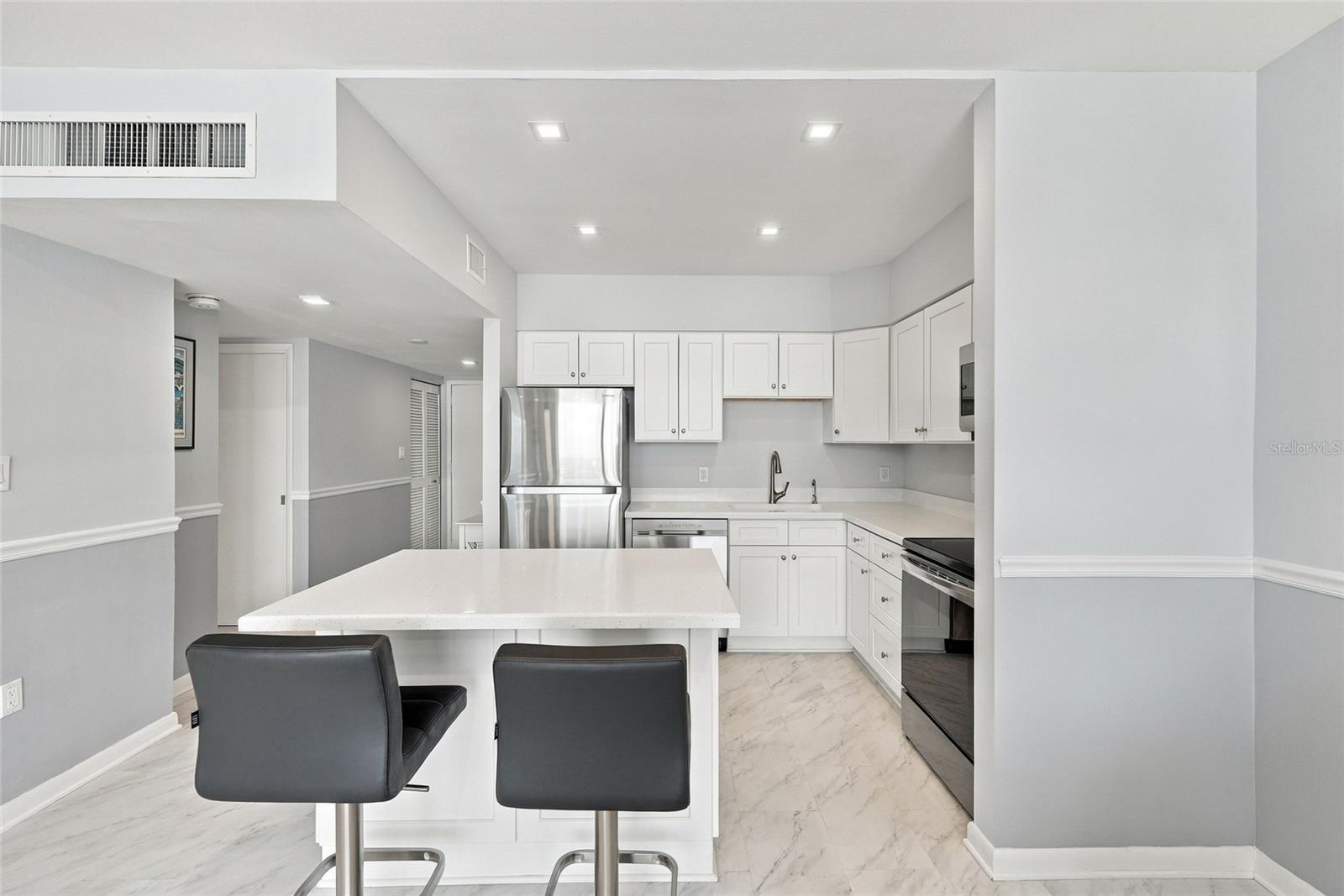 Updated kitchen with white cabinetry, stainless steel appliances, and an island with two dark stools.