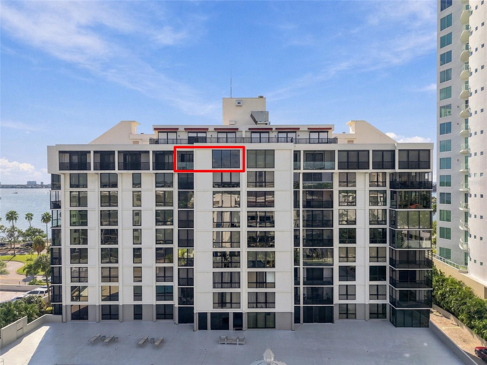 Waterfront condominium building with unit 1006 outlined in red and bay water visible beside it.