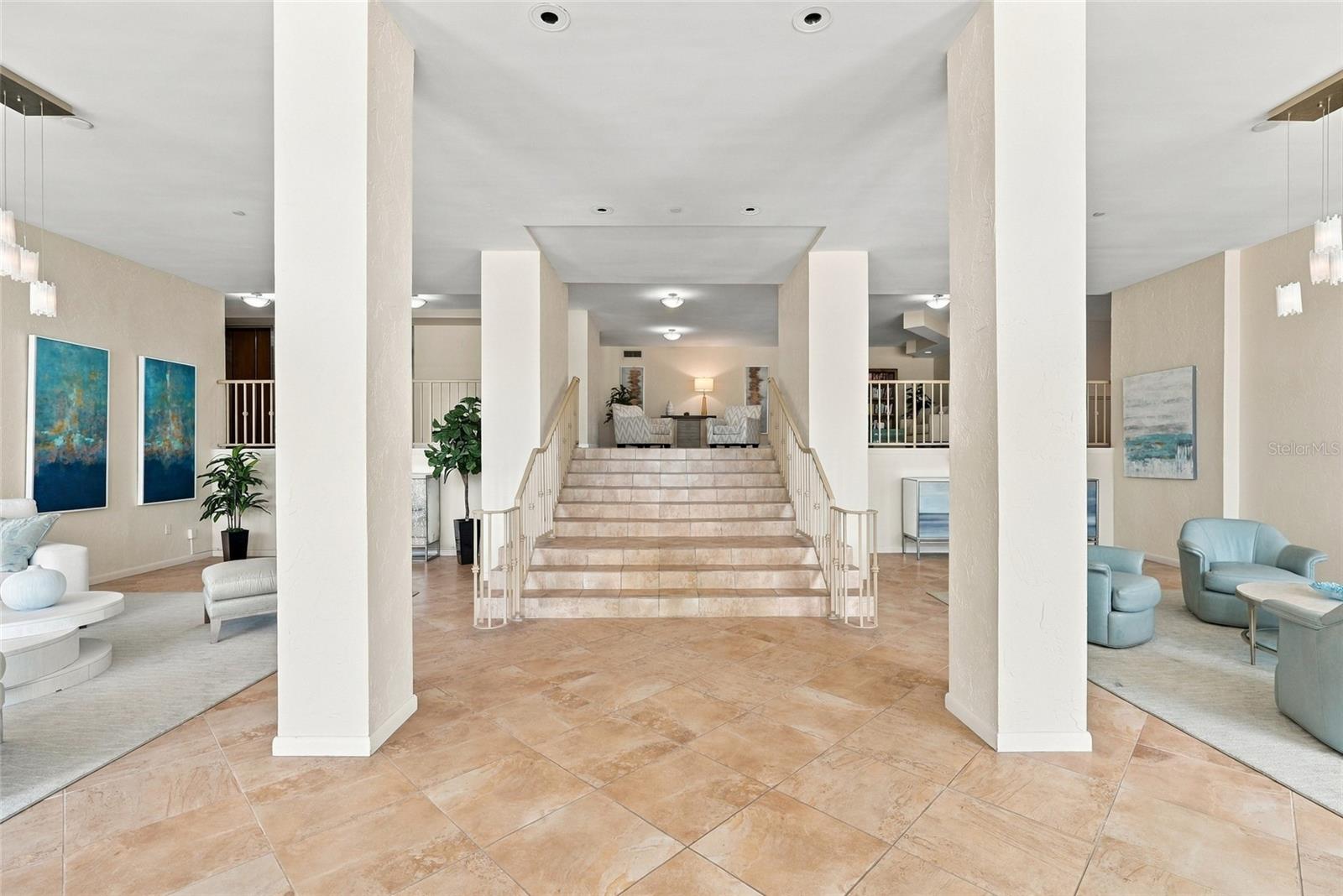 Condominium lobby with a central staircase, white columns, and blue seating.