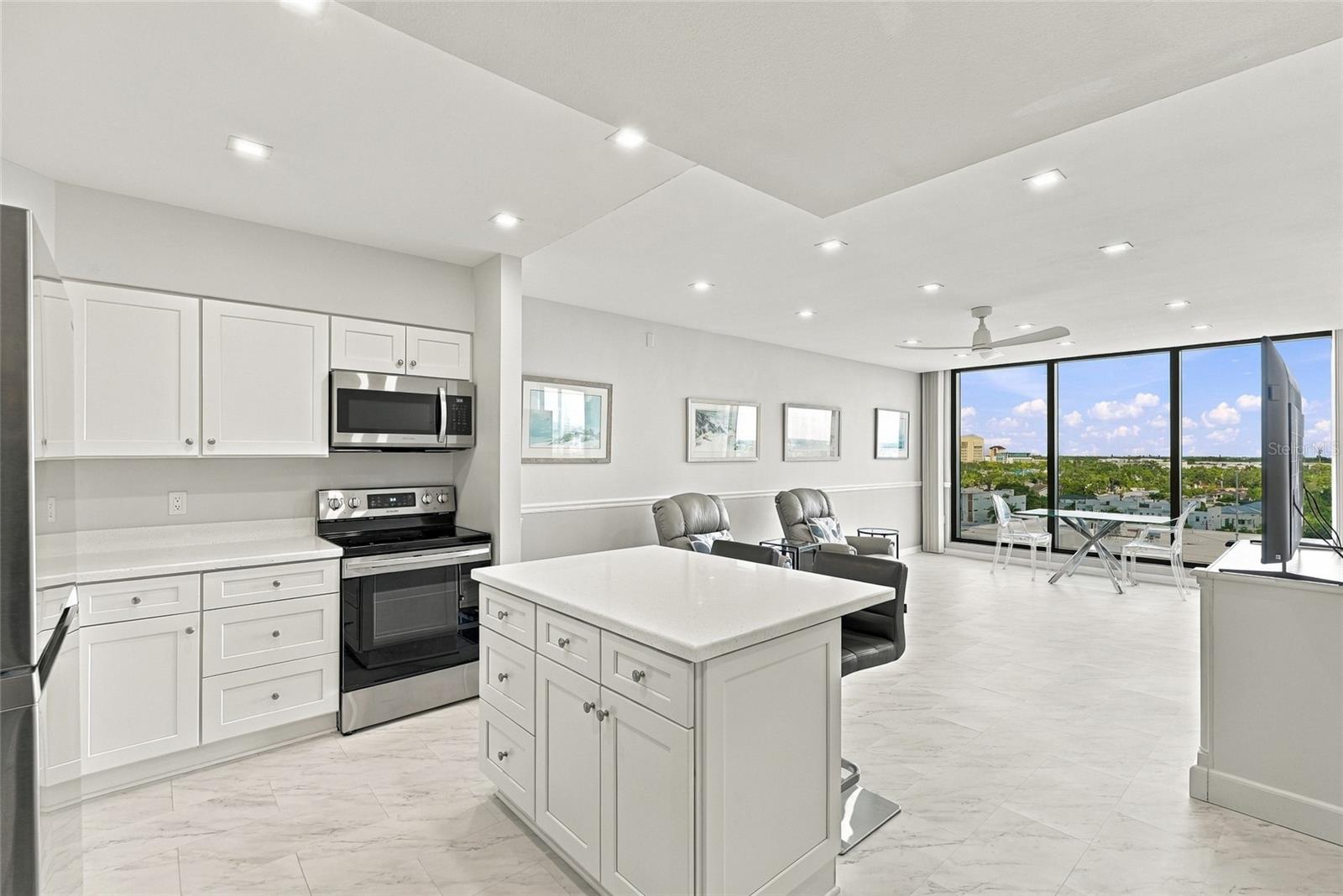 Open-plan condo kitchen with a large white island and floor-to-ceiling windows overlooking the city and water.