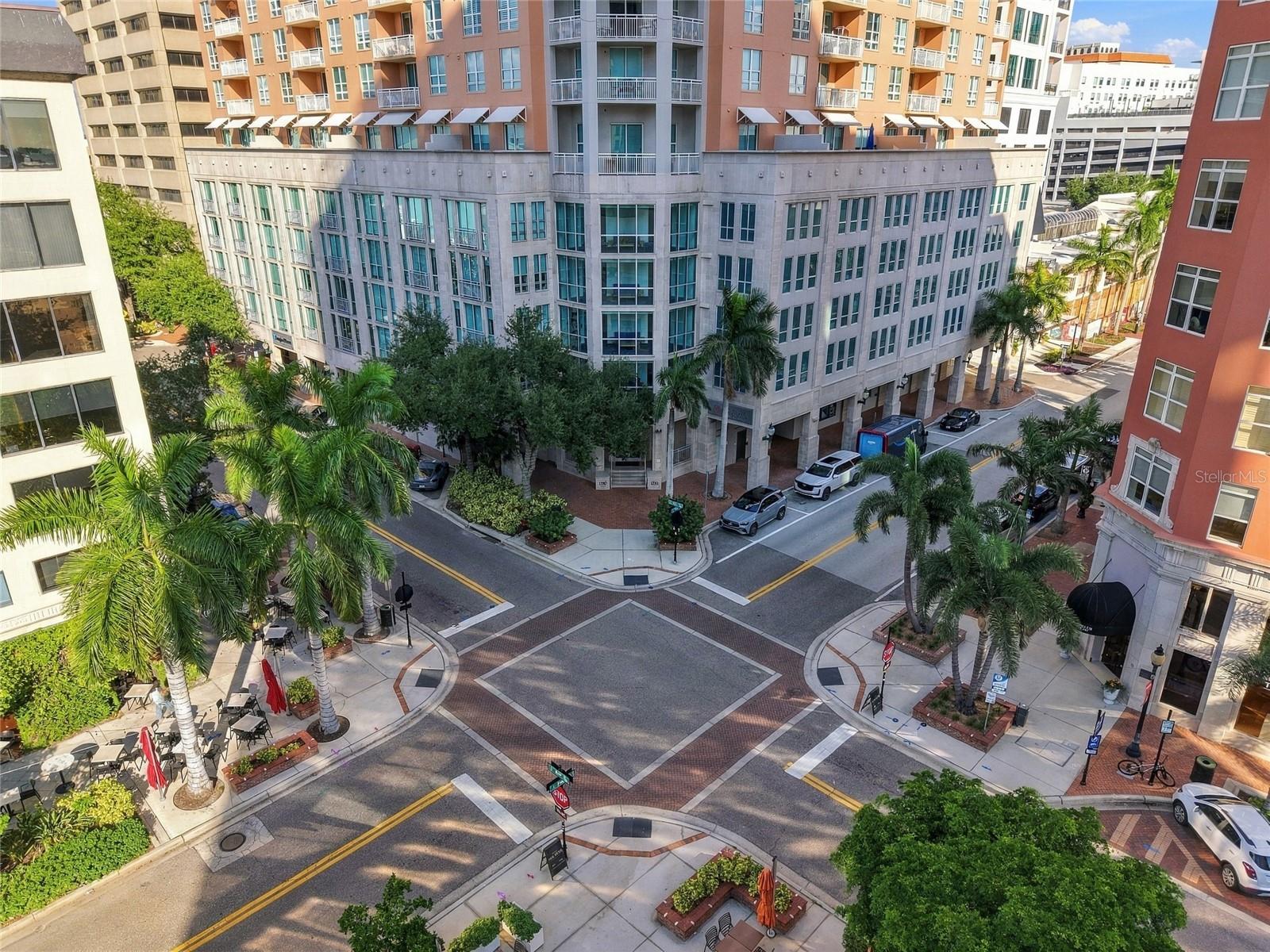 Aerial view of a downtown condominium with balconies above a palm-lined street intersection.