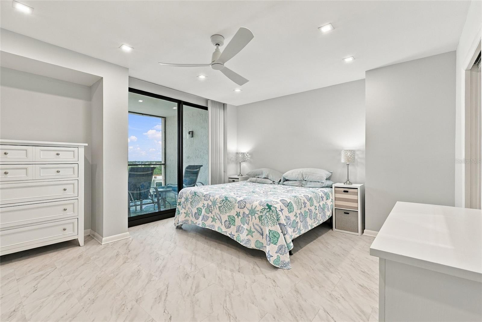 Bedroom with seashell-patterned bedding, marble-look tile flooring, and sliding glass doors to a balcony.