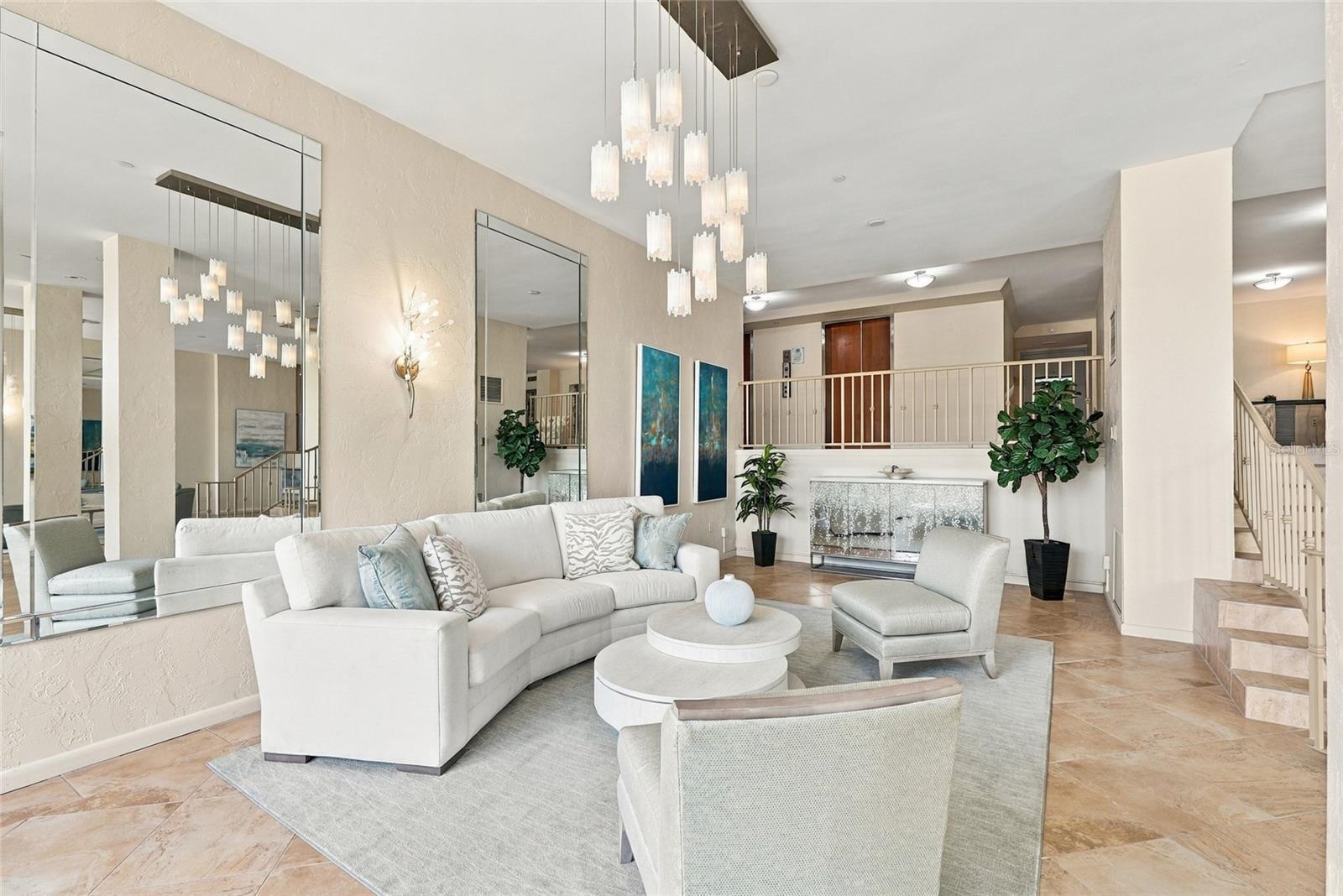 Condominium living room with white seating, mirrored walls, pendant lights, and a fireplace.