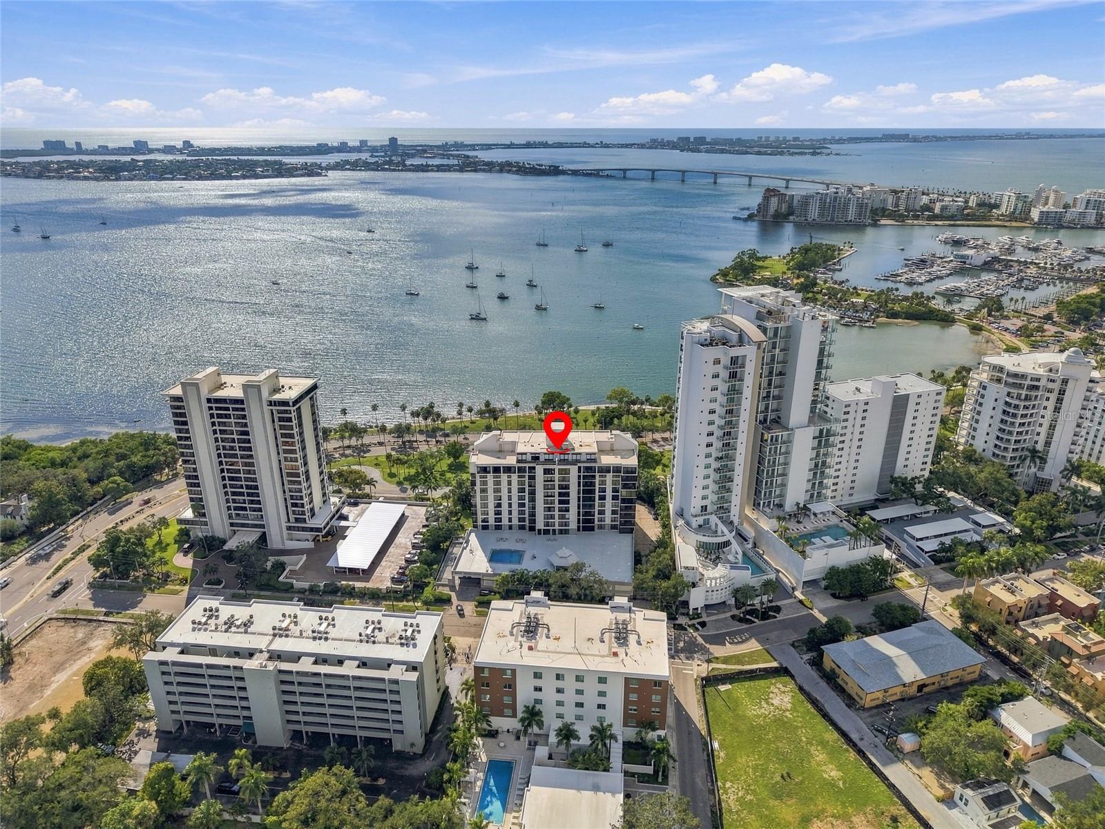 Aerial view of a marked condominium beside Sarasota Bay, marina, bridge, and high-rises.