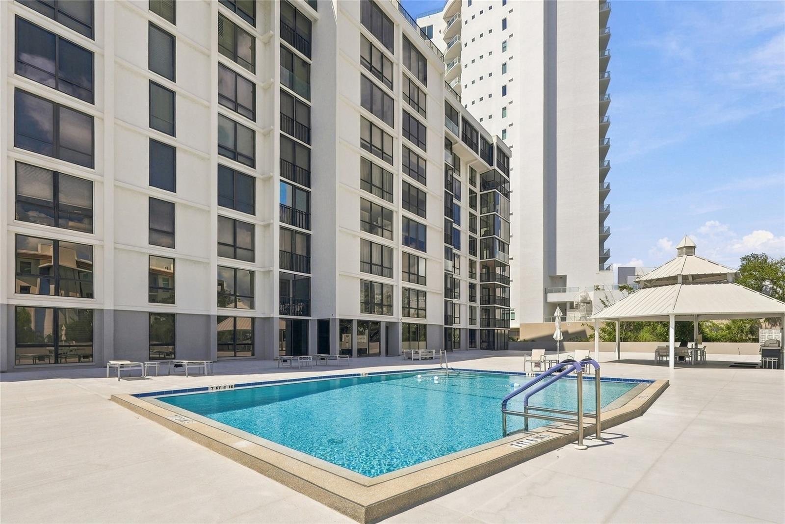 Condominium pool beside a high-rise building, with a sun deck and covered gazebo.