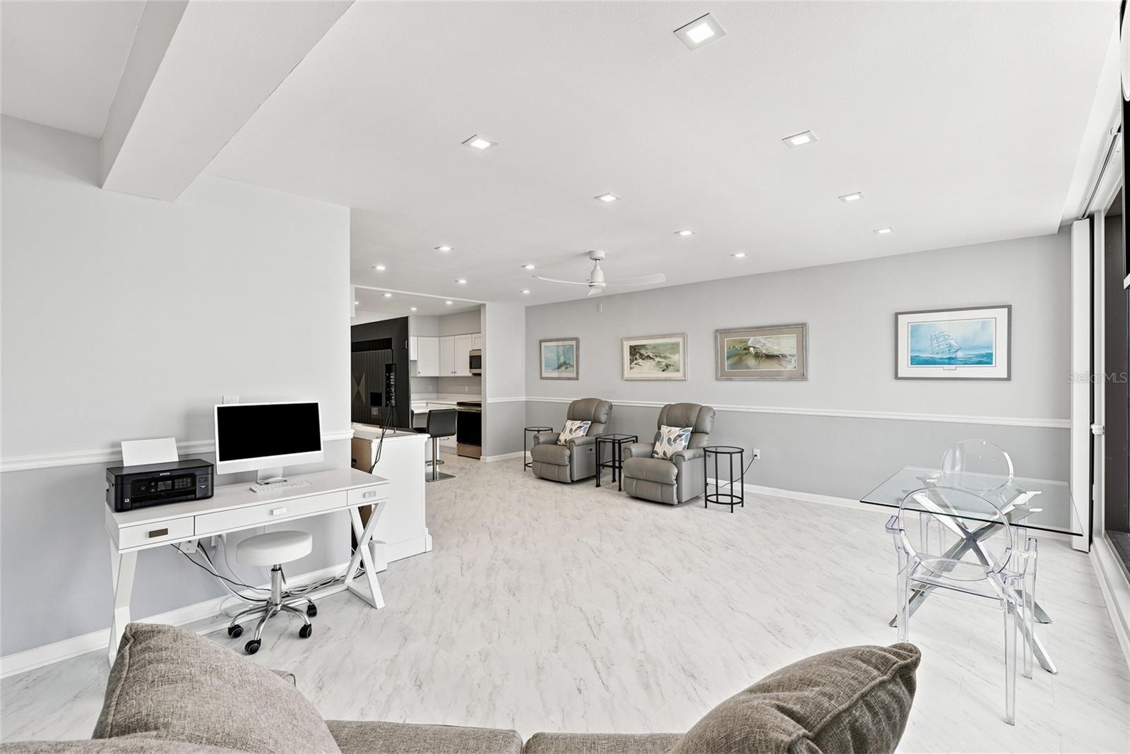 Open-plan condo living area with marble-look floors, gray recliners, a desk, and a glass dining table.