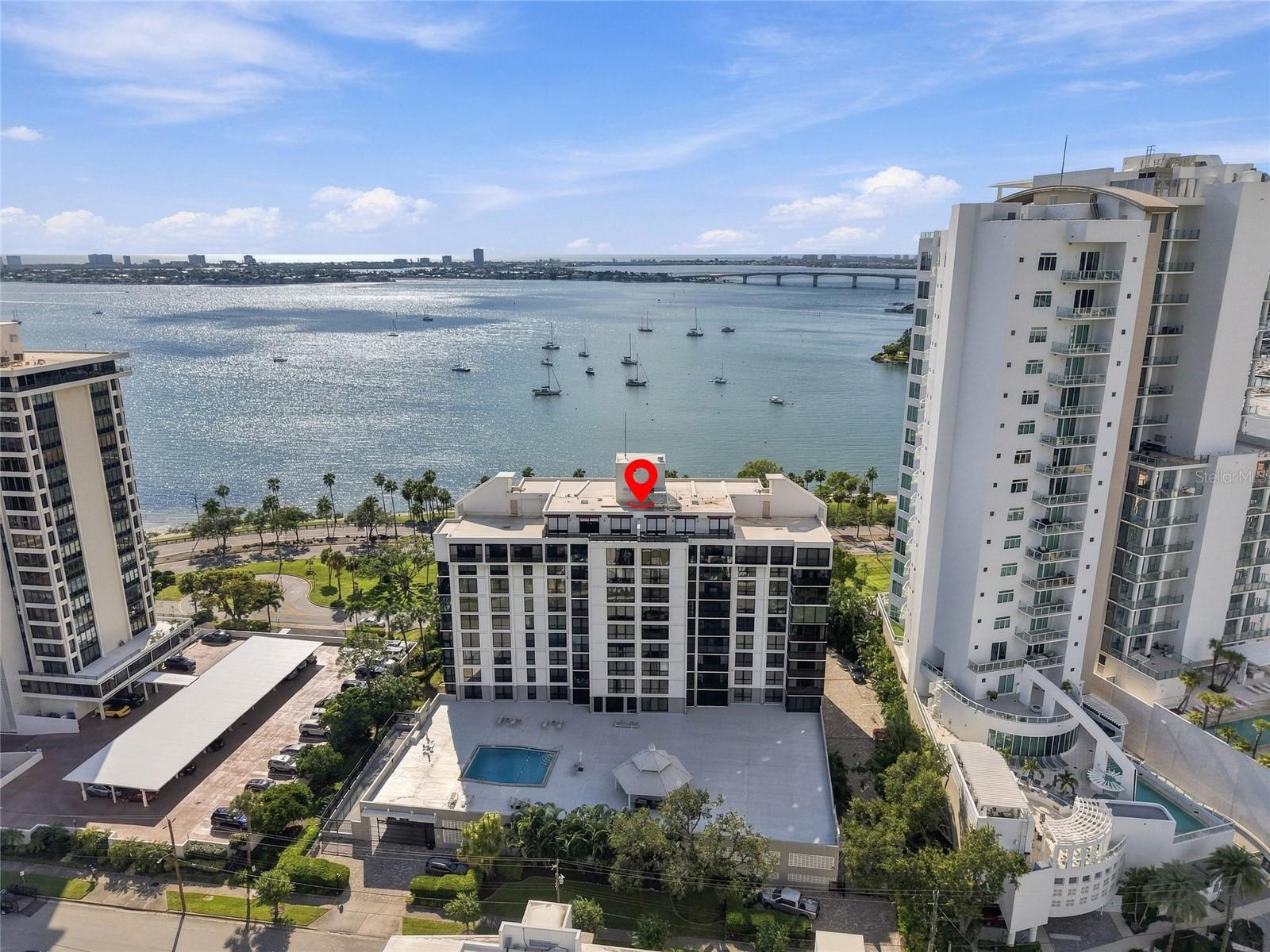 Waterfront condominium complex beside Sarasota Bay, with boats, a bridge, and a red location pin.