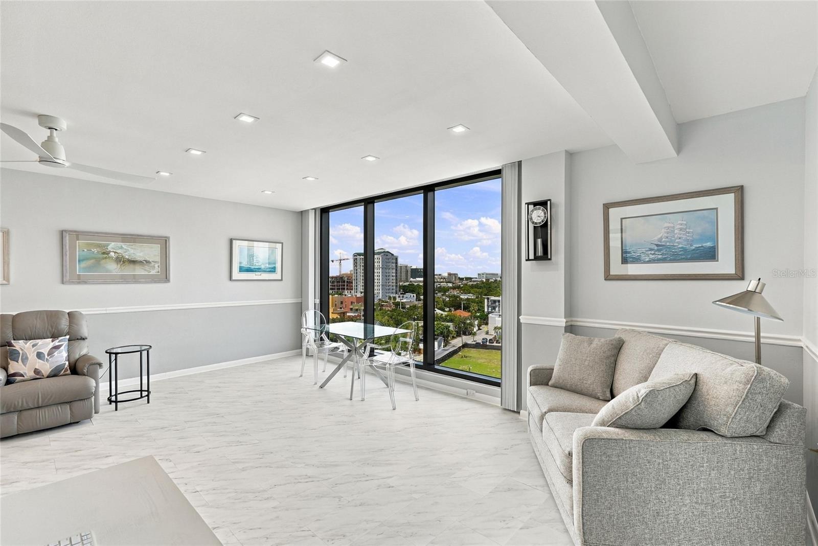 Living room with gray sofas and floor-to-ceiling windows overlooking downtown buildings.