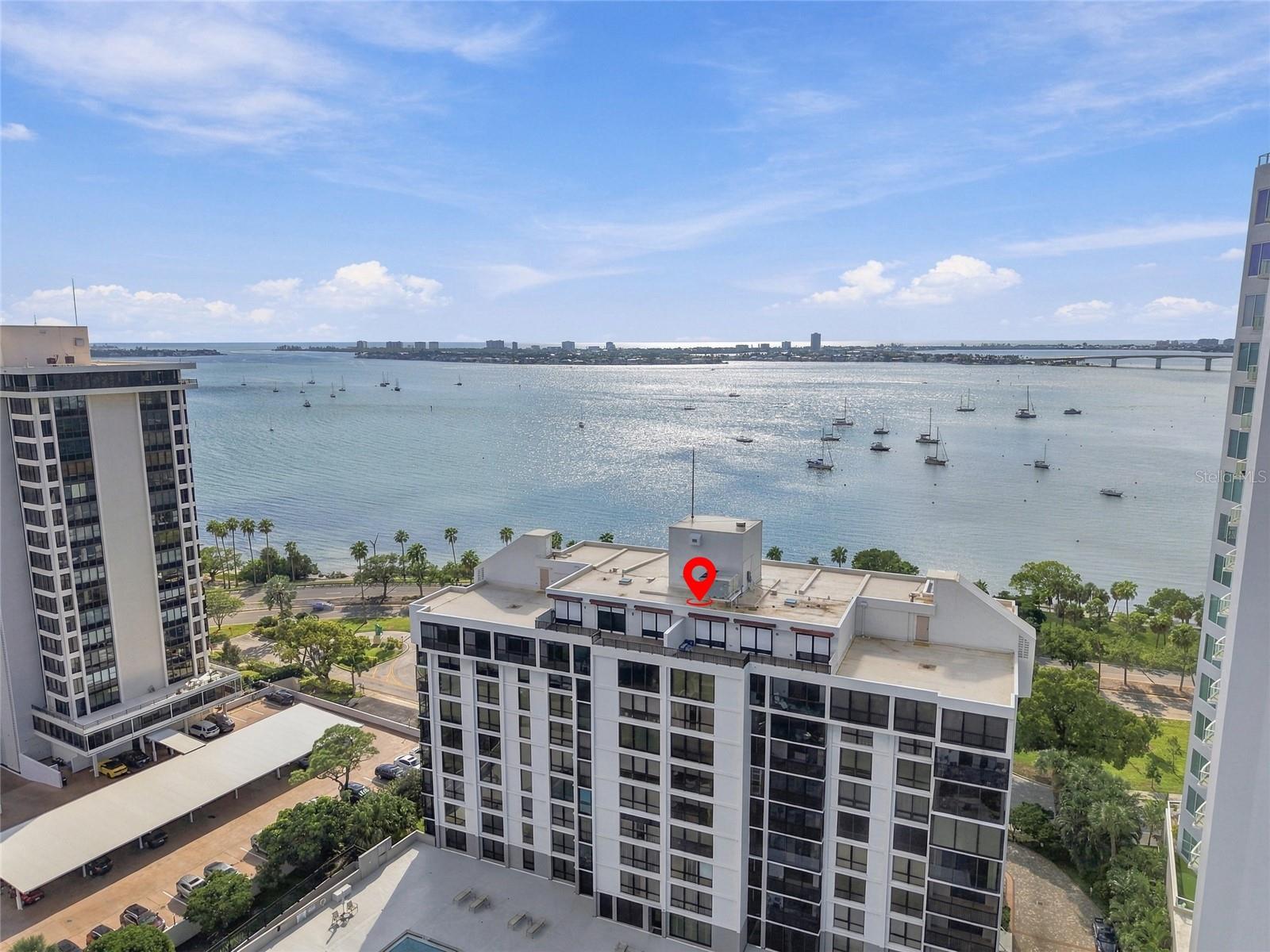 Waterfront condominium buildings overlook a bay dotted with boats, with a bridge in the distance.