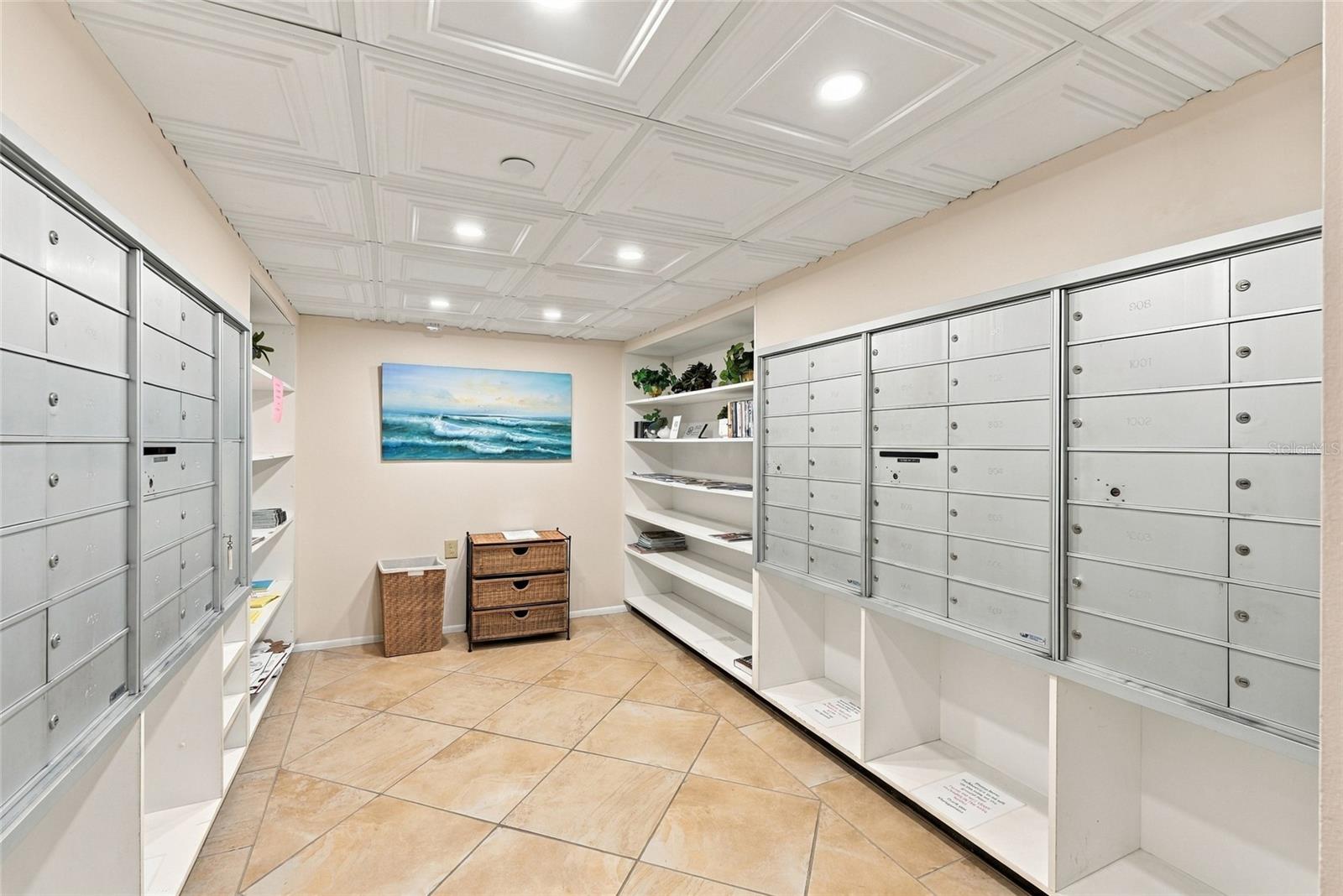 Condominium mailroom with rows of metal mailboxes, open shelving, and a tiled floor.