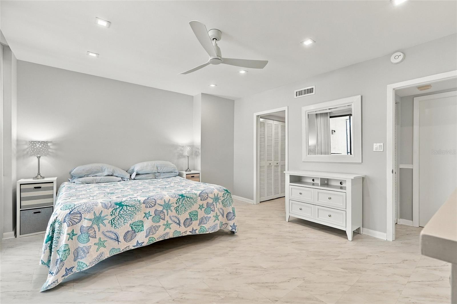 Bedroom with sea-life patterned bedding, white dresser, and pale marble-look flooring.