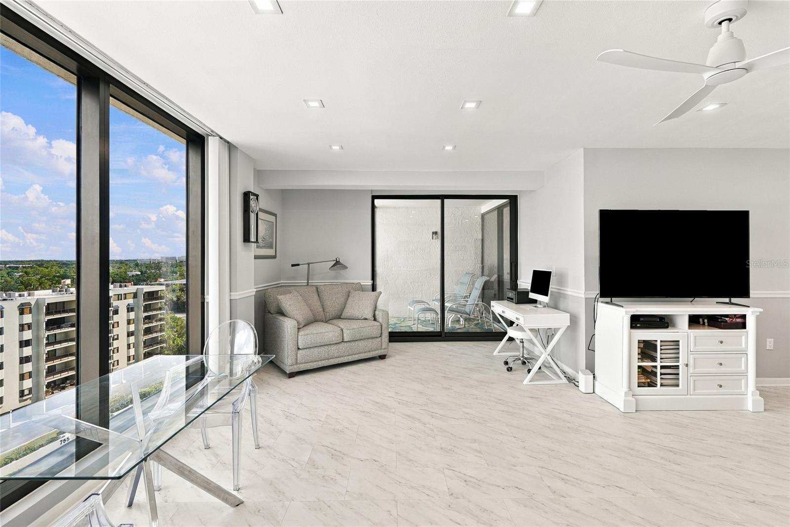High-rise condo living room with expansive windows, a gray sofa, glass dining table, and balcony doors.